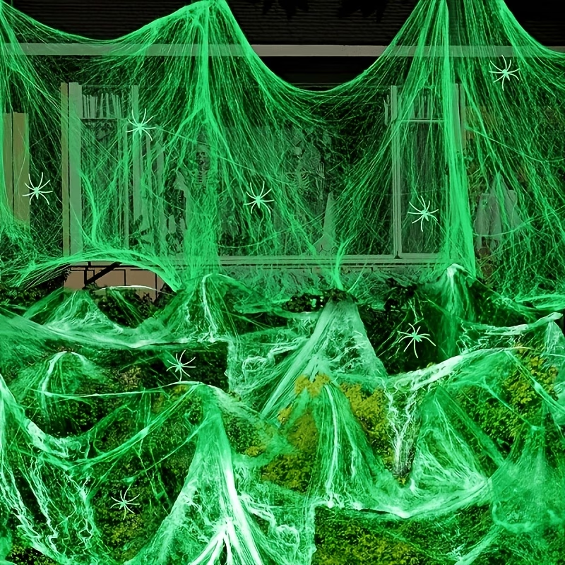 Illustrative green glow-effect stretch-web styling display. Decorative spiders and other background props illustrate styling; the item sold is one web pack.