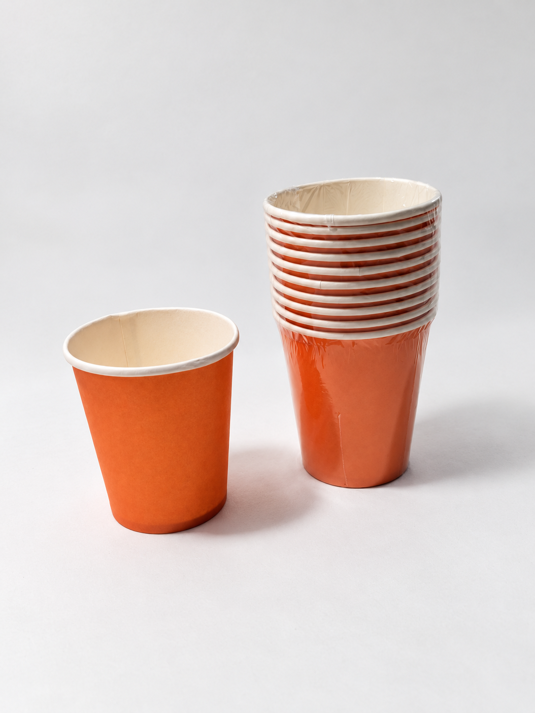 Orange paper cups showing a wrapped pack beside one display sample; sold as a pack of ten cups; actual-stock photo with background and lighting retouched