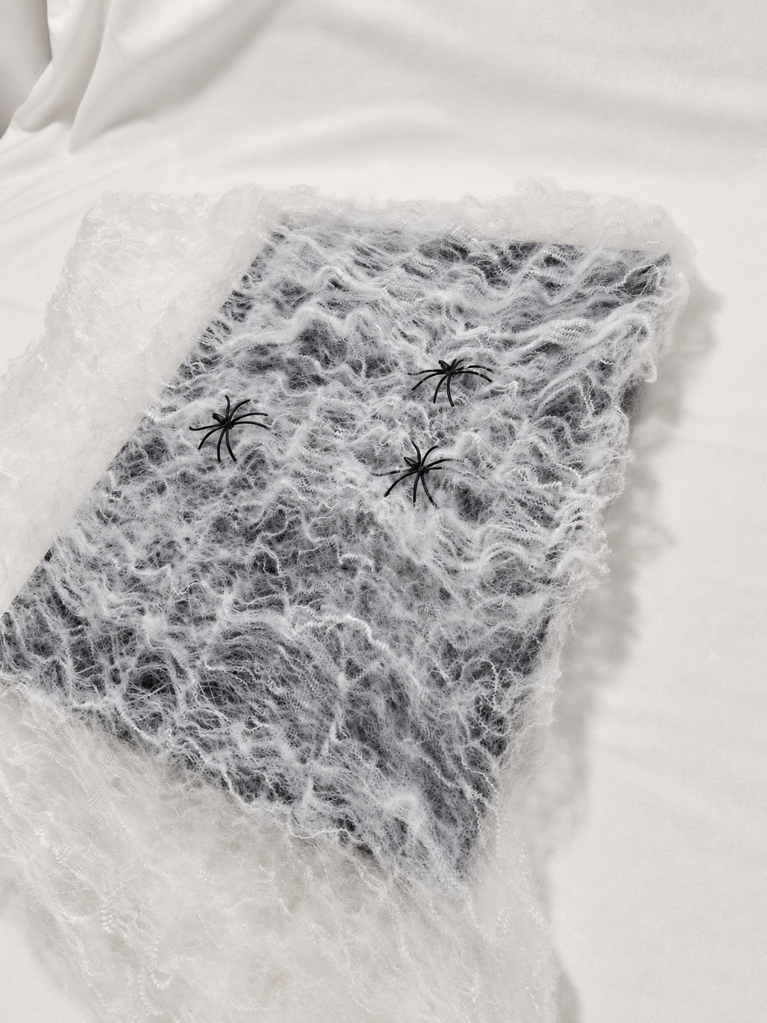 White decorative spider web spread with three black spiders, photographed from actual stock; background and lighting retouched