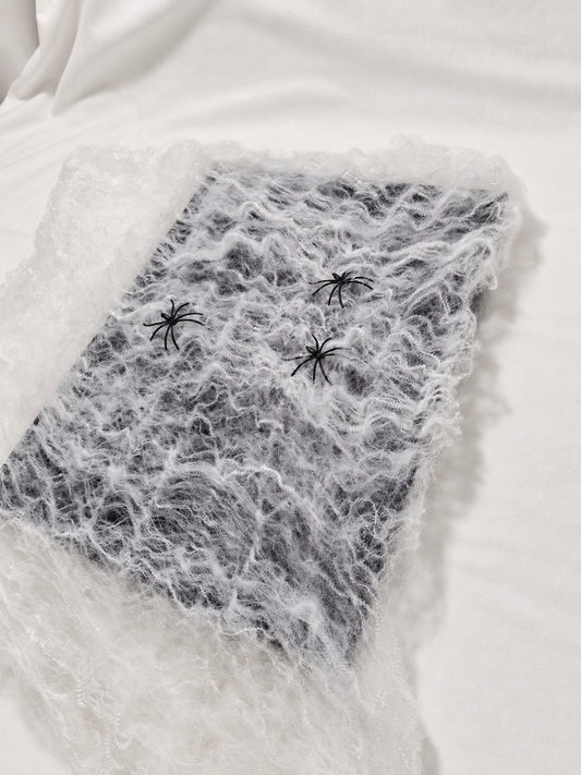 White decorative spider web spread with three black spiders, photographed from actual stock; background and lighting retouched