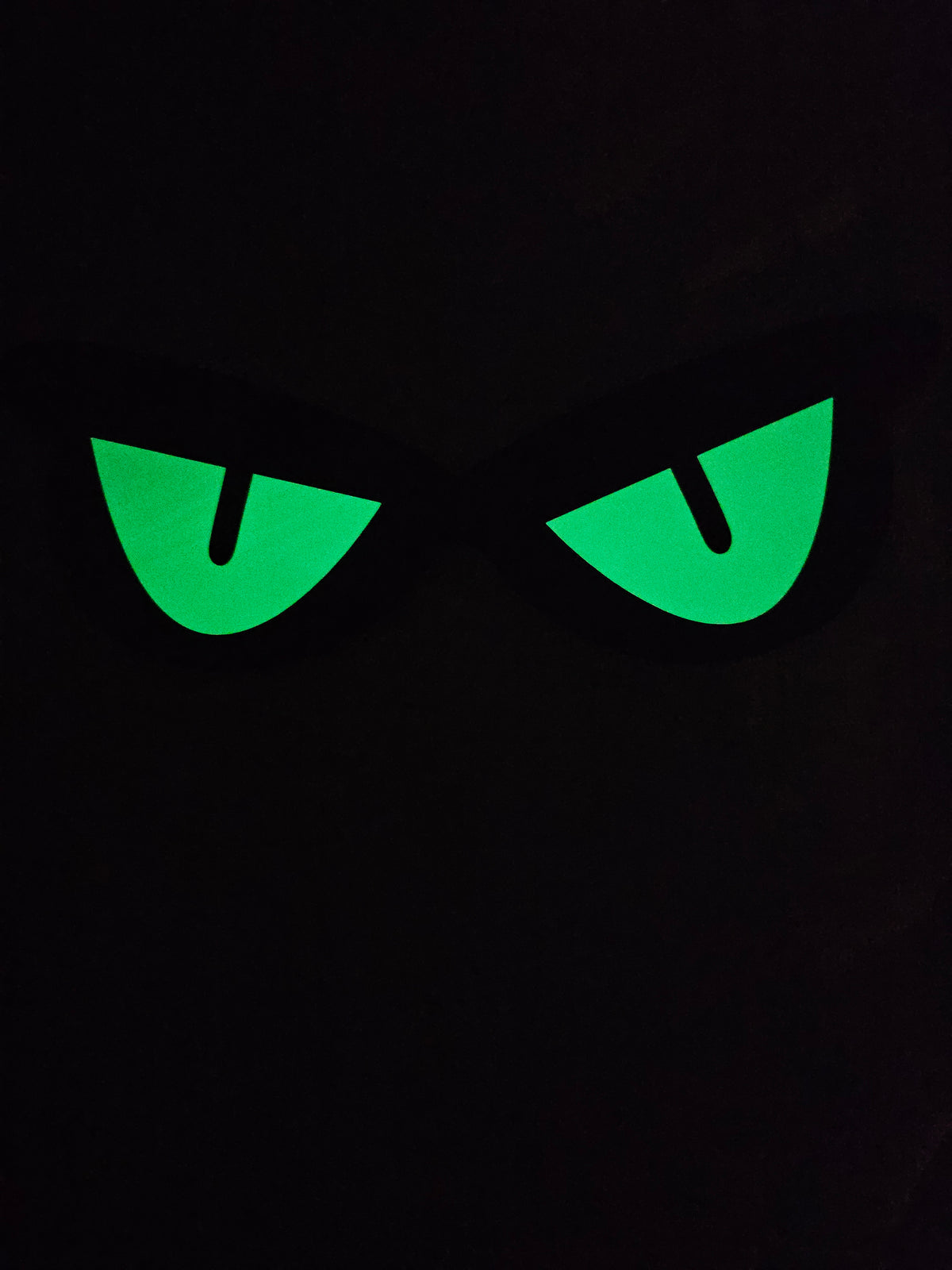 Unedited actual-stock night photograph of one Somebody’s Watching eye decoration showing its captured green glow. Original exposure retained; brightness and duration are not guaranteed. Four decorations per sale set.