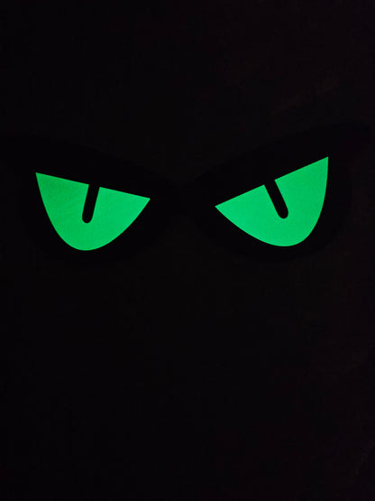 Unedited actual-stock night photograph of one Somebody’s Watching eye decoration showing its captured green glow. Original exposure retained; brightness and duration are not guaranteed. Four decorations per sale set.